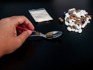 The hand of a person taking drug from a spoon with a syringe and pills of different sizes, shapes...