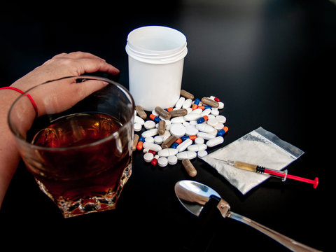 One person. A glass of whiskey on their hand. Pills of different sizes, shapes and colors, drugs and syringes Concept of drugs and alcohol