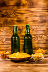 Two bottles of beer and different snacks on wooden table