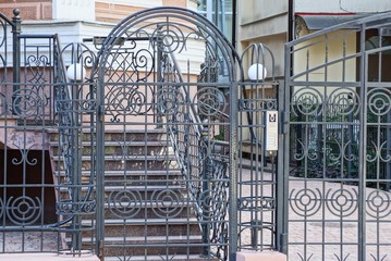 The door and part of the black fence of steel rods in a knitted pattern