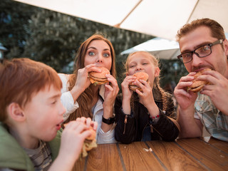 hungry family eating hamburgers, sitting at a table in a fast food restaurant