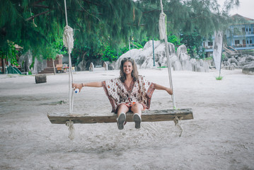 Happy young woman swinging on the swing at tropical beach