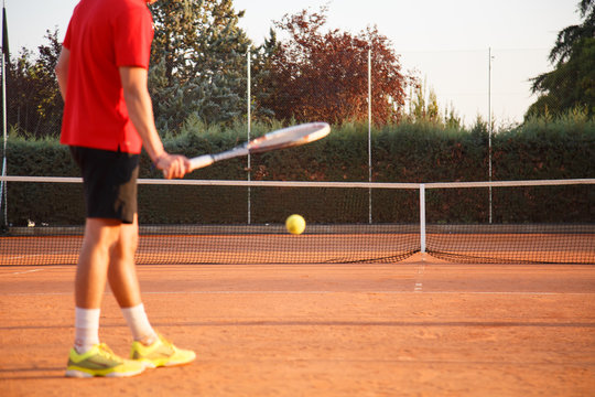 Defocused professional man tennis player playing on the court in the afternoon and bouncing the ball against the ground with the racket. 