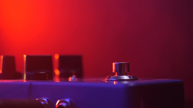 Extremely close up of guitarist foot in sneakers pressing button for effect electro guitar pedal. Red neon light in night club during show concert . 4k