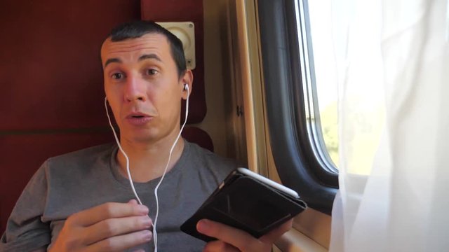 man listening to the music on the train rail car coupe compartment travel. slow motion video. man with a smartphone at the window of a train in a car travel internet social media web lifestyle. man