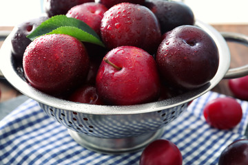 Colander with ripe juicy plums on table