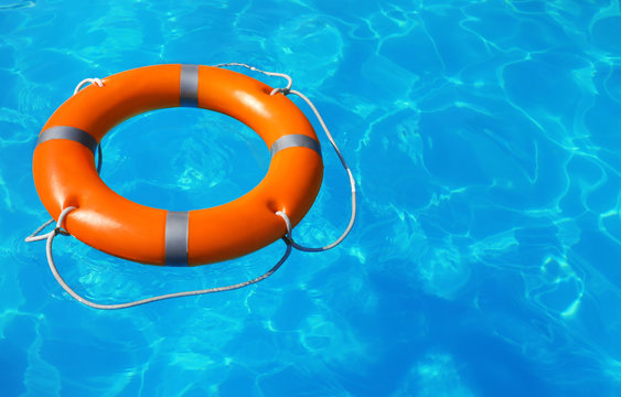 Lifebuoy floating in swimming pool on sunny day. Space for text