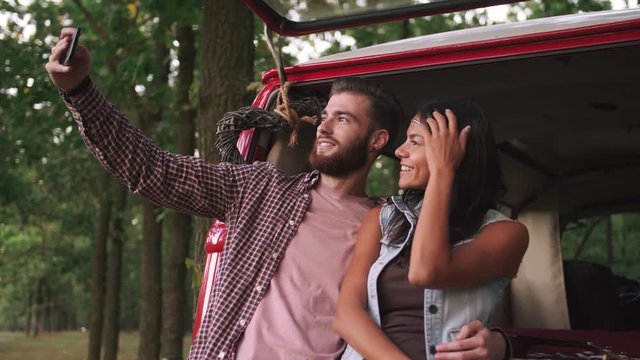 Young cheerful happy young couple doing selfie near retro bus in forest and having some fun, slow motion