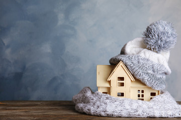 Plywood toy house with warm hat, scarf and space for text against color background. Heating system