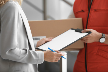 Young woman signing documents after receiving parcel from courier indoors