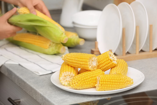 Plate with ripe corn cobs and blurred woman on background