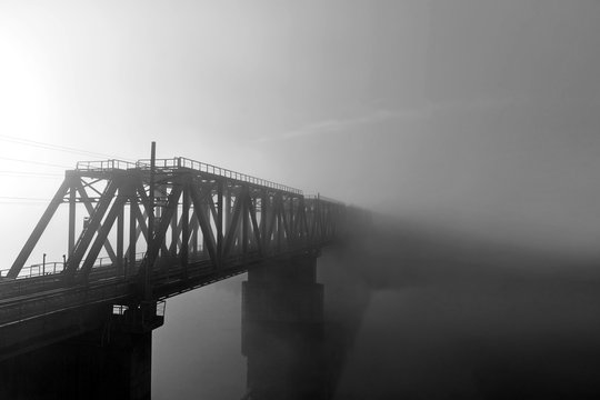 The railway bridge over the river in the fog. Railway in the morning without people. Black and white photography