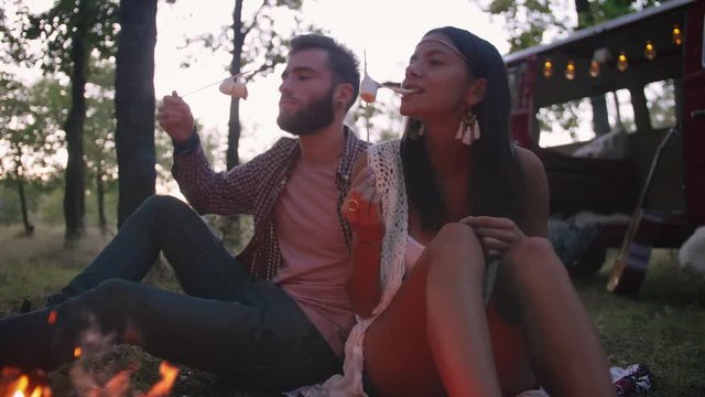 Beautiful young couple roasting marshmallows over a campfire while enjoying their road travel