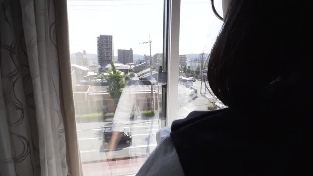 Short haired female lady opening up the curtain revealing the bright view outside.