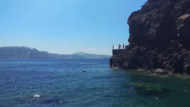 View 2: People jumping of the cliff into the crystal clear Mediterranean waters in Amoudi Bay. Beautiful fishing village below Oia, SANTORINI, GREECE.