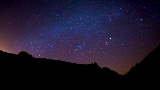 timelapse of blue sky and stars moving while a silhouette of a mountain sits in the foreground