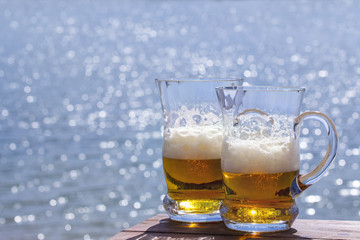 Two mugs of fresh beer on the table against the sea