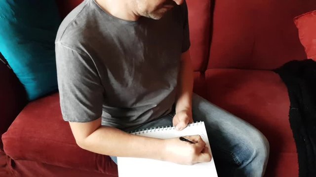 Male with a partially amputated index finger on his right hand sat down holding a pen and pad  writing a to do list.