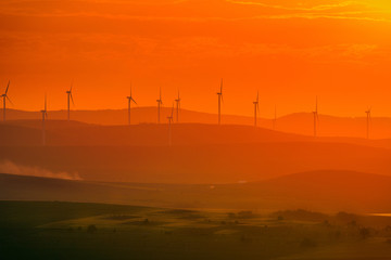 Aeolian turbines placed on hills used to produce ecological green electricity shot at sunset with a field in the foreground