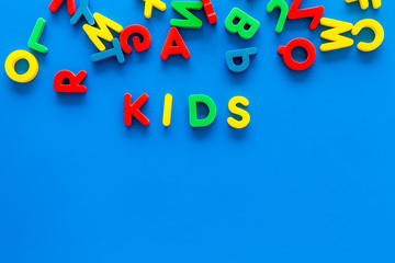 Early childhood development concept. Word kids written by plastic letters of toy alphabet on blue background top view copy space