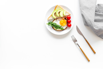 Fototapeta na wymiar Healthy hearty breakfast. Fried eggs with vegetables near toast with avocado on white background top view copy space
