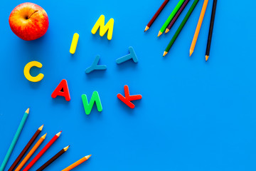 Primary school concept. Letters of english alphabet, book, apple and color pencils on blue background top view