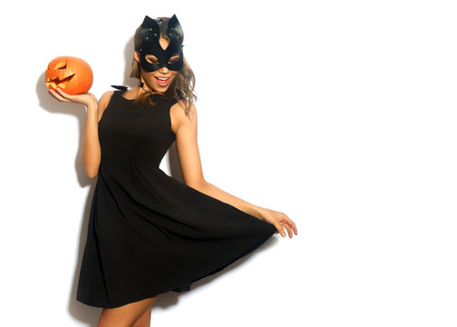 Happy young women in little black dress with Halloween pumpkin and in cat mask over white background