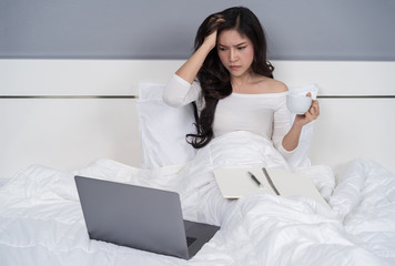stressed  woman thinking and working with laptop computer on a bed