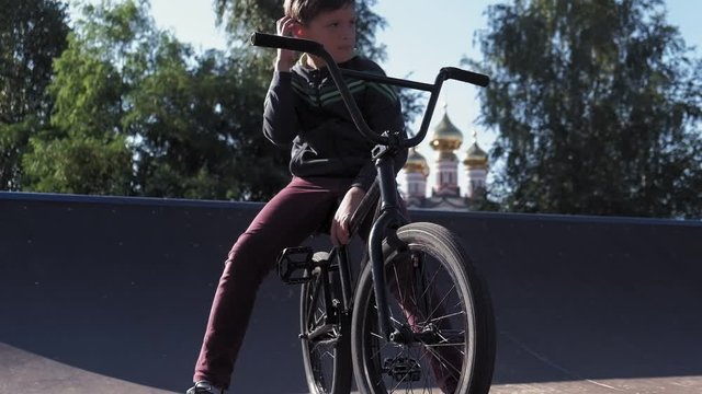 A boy is riding BMX cycling tricks in a skateboard park on a sunny day. Super Slow Motion