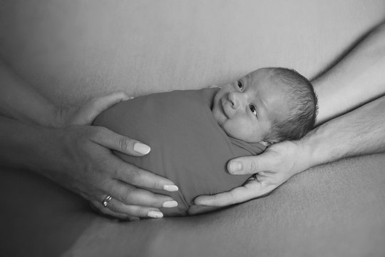 black and white photo: portrait of newborn baby lying on the hands of parents