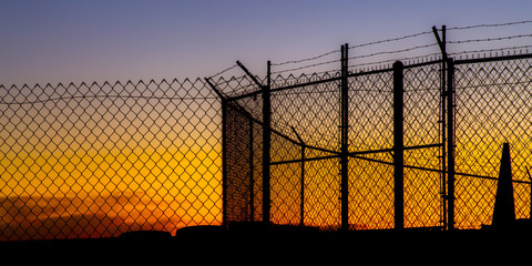 Mesh wire fence and barbeb wire at sunset - Powered by Adobe