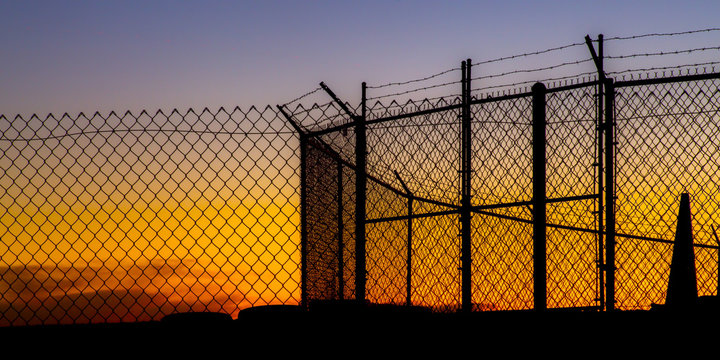Mesh wire fence and barbeb wire at sunset