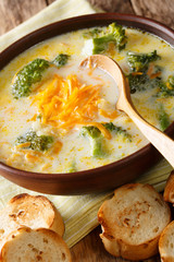 Delicious broccoli cheddar cheese soup in a bowl with toasted bread closeup. vertical