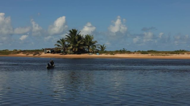 Static shot of a lone fisherman rowing a small wooden fishing boat on the Itaunas River in Brazil