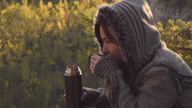 A brunette girl is drinking tea in nature. Rest day at weekends. Sunny autumn day. Slow Motion Picture