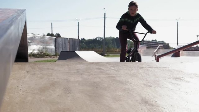 A boy is riding BMX cycling tricks in a skateboard park on a sunny day. Super Slow Motion