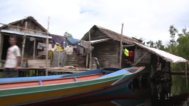 Passing houses on stilts with colorful boats in the jungle of Borneo