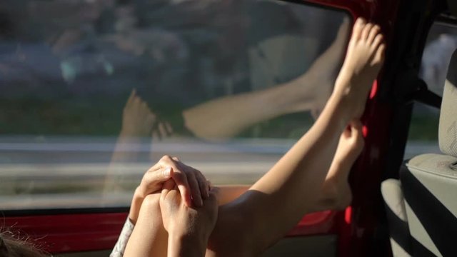 A young redhead woman enjoys traveling by car throws her legs on the window. Slow motion.
