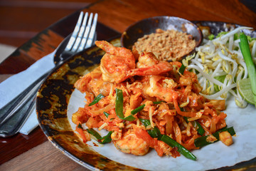 Thai food, stir fry rice noodles with shrimps, tofu, vegetable and crushed peanuts or pad thai on wooden table background, pad thai is a popular Thai street food among tourists visiting Thailand.