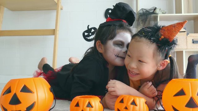 Two asian girl dressed as witch and ghost lying on the floor and talking together in a room decorated for Halloween