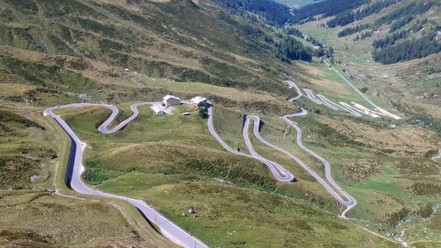 Slow panning aerial shot over the tight serpentine turns of the Spl&uuml;gen pass in the Switzerland. The road twists and curves up the through the lush green alpine hills.