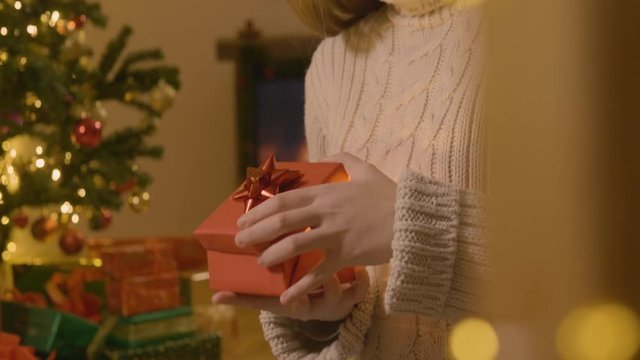 Happy teenage girl opening a Christmas present in front of a Christmas tree