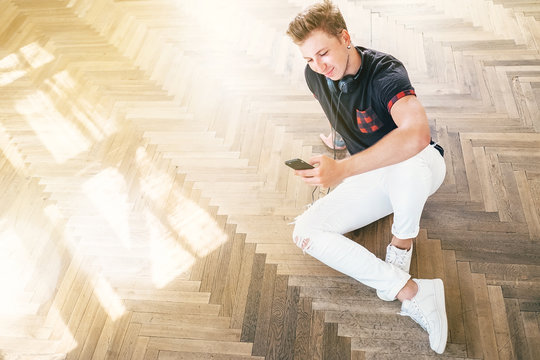 Young man using his smartphone with headphones, listen the music and sit on the floor