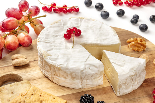 A closeup photo of Camembert cheese with fruits and nuts, shot on a white background