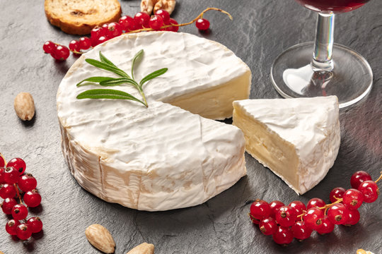 A photo of Camembert cheese with a glass of red wine, fruits and nuts, shot on a black background with copy space