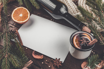 Mug of hot mulled wine, a bottle of red wine, spruce branches, cinnamon, aniseed tree, orange on a wooden background. A cozy, winter evening. Winter drinks. Copy space