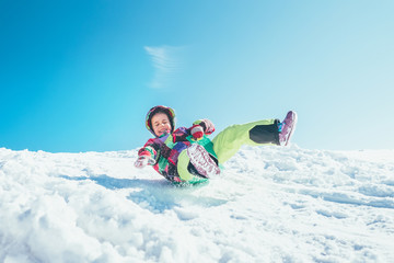 Happy little girl slides down from the snow slope. Enjoying the winter sledding time