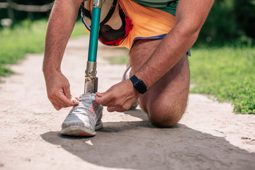 Low angle of a man with prosthesis tying his shoes