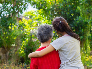 Back view of young woman hugging her grandmother in garden.
