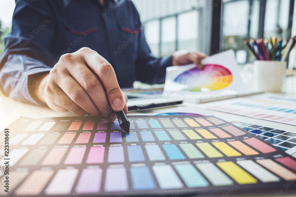Poster Image of male creative graphic designer working on color selection and drawing on graphics tablet at workplace with work tools and accessories